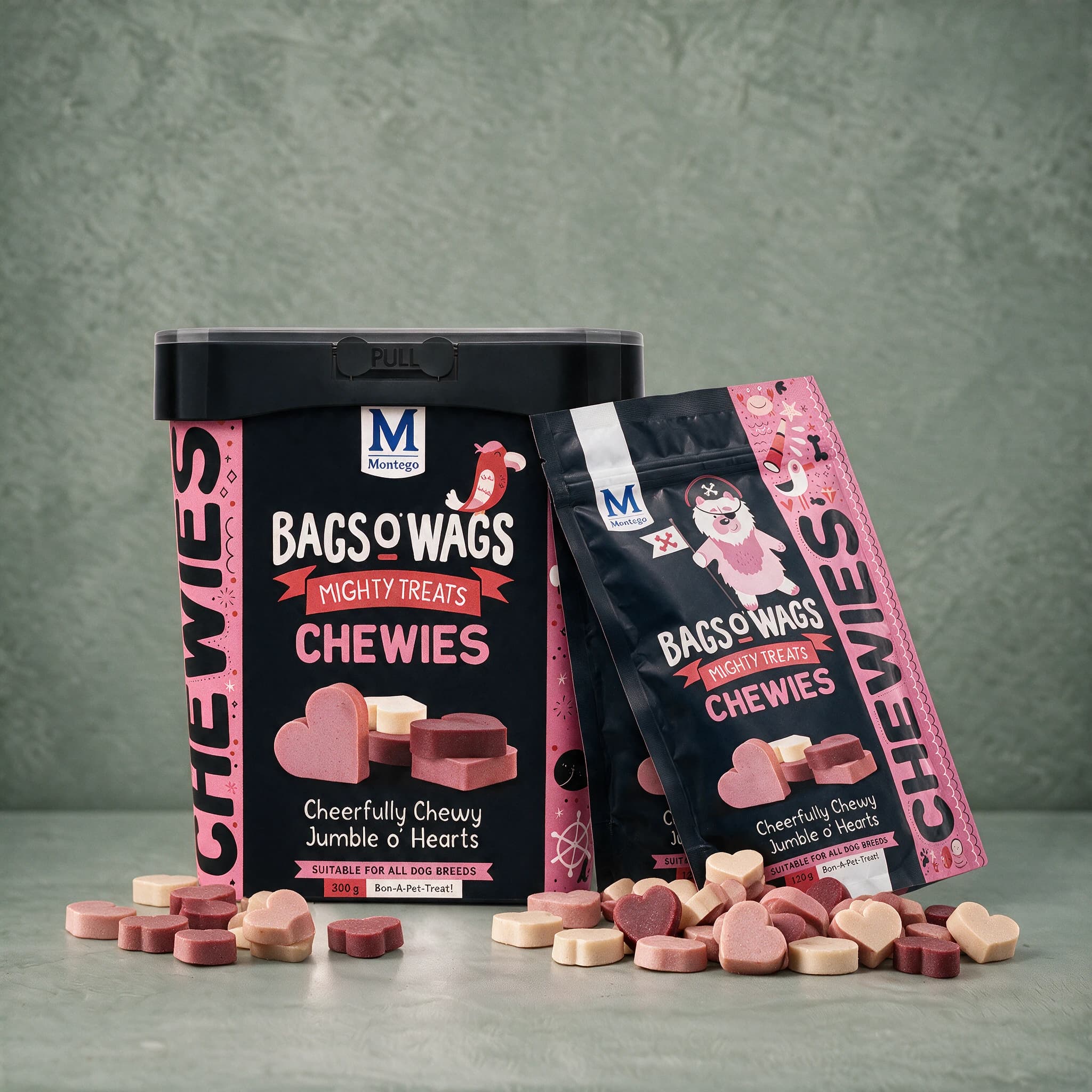 A black plastic 300 g tub of Bags O' Wags Mighty Treats Chewies Jumble o' Hearts standing beside a black 120 g pouch of the same flavour, both packs against a plain sage green studio background with heart-shaped treats scattered at their base.