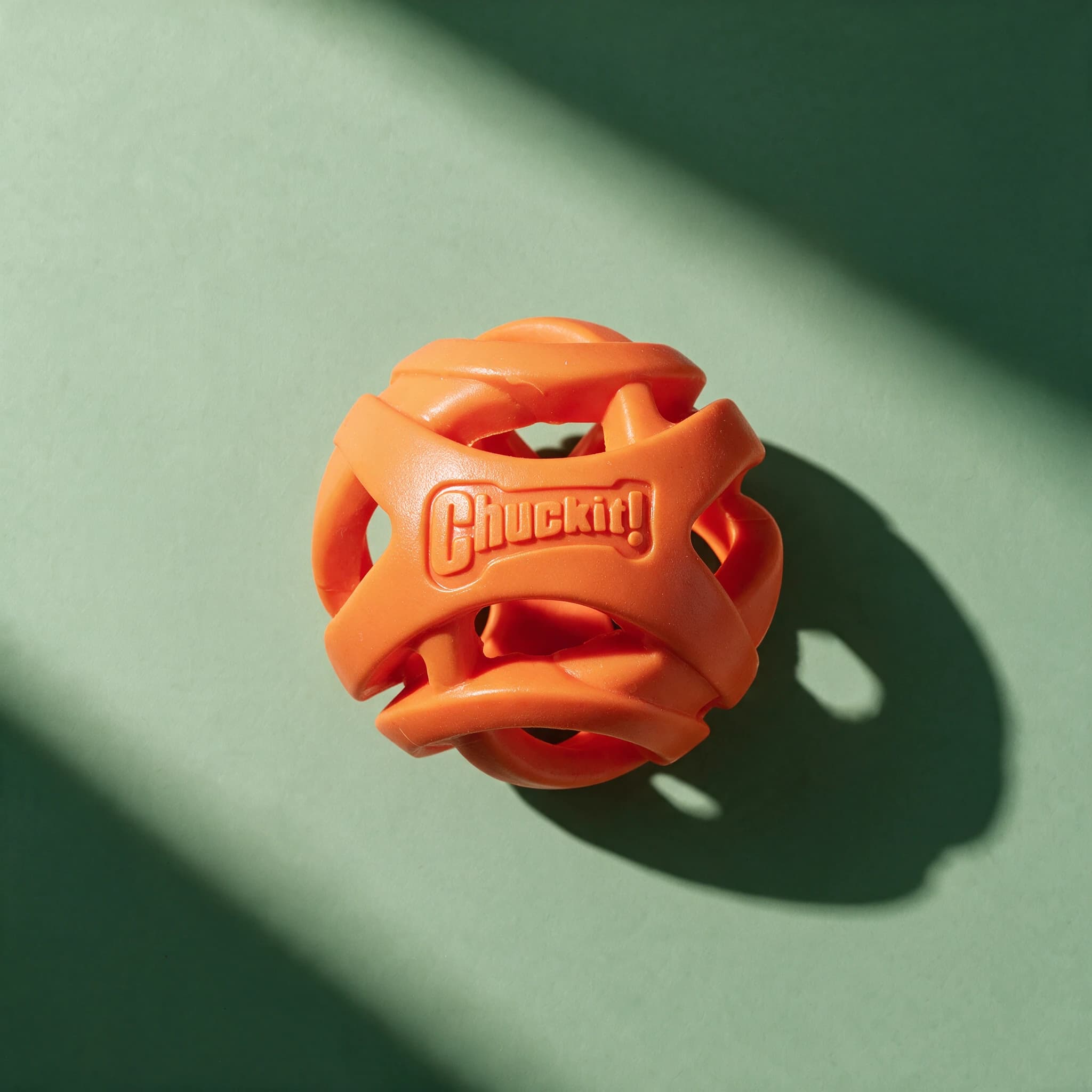 An orange Chuckit! Air Fetch Ball, showing its openwork lattice design and embossed "Chuckit!" logo, against a plain green background.