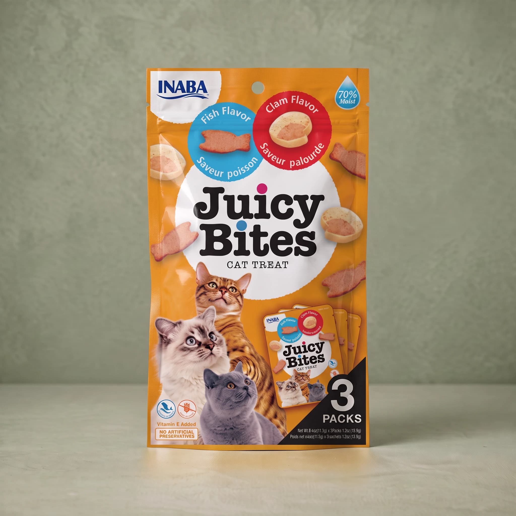 Amber-orange INABA Juicy Bites cat treat pouch in the Fish and Clam flavours, with a blue 'Fish Flavor' roundel showing a fish-shaped treat and a red 'Clam Flavor' roundel showing a clam-shaped treat, a '70% Moist' droplet flash, photographs of three cats, and a '3 PACKS' panel.