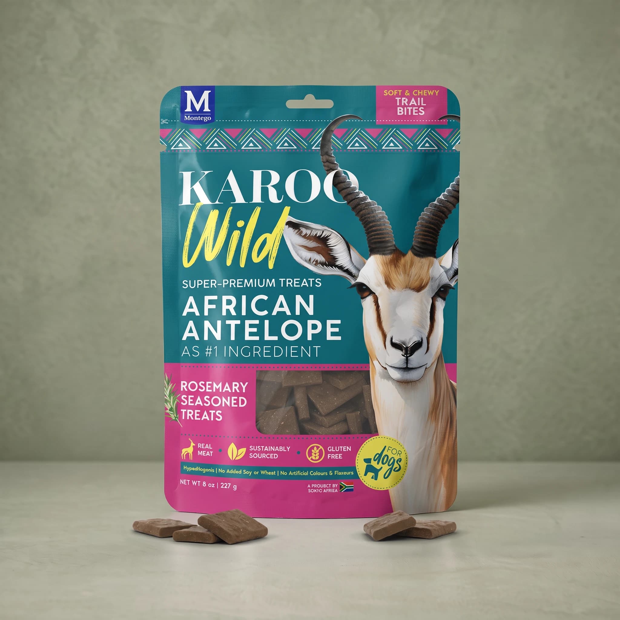 The same teal and magenta Karoo Wild Rosemary Trail Bites pouch standing upright against a plain sage green background, with small square dark brown treats scattered at its base.