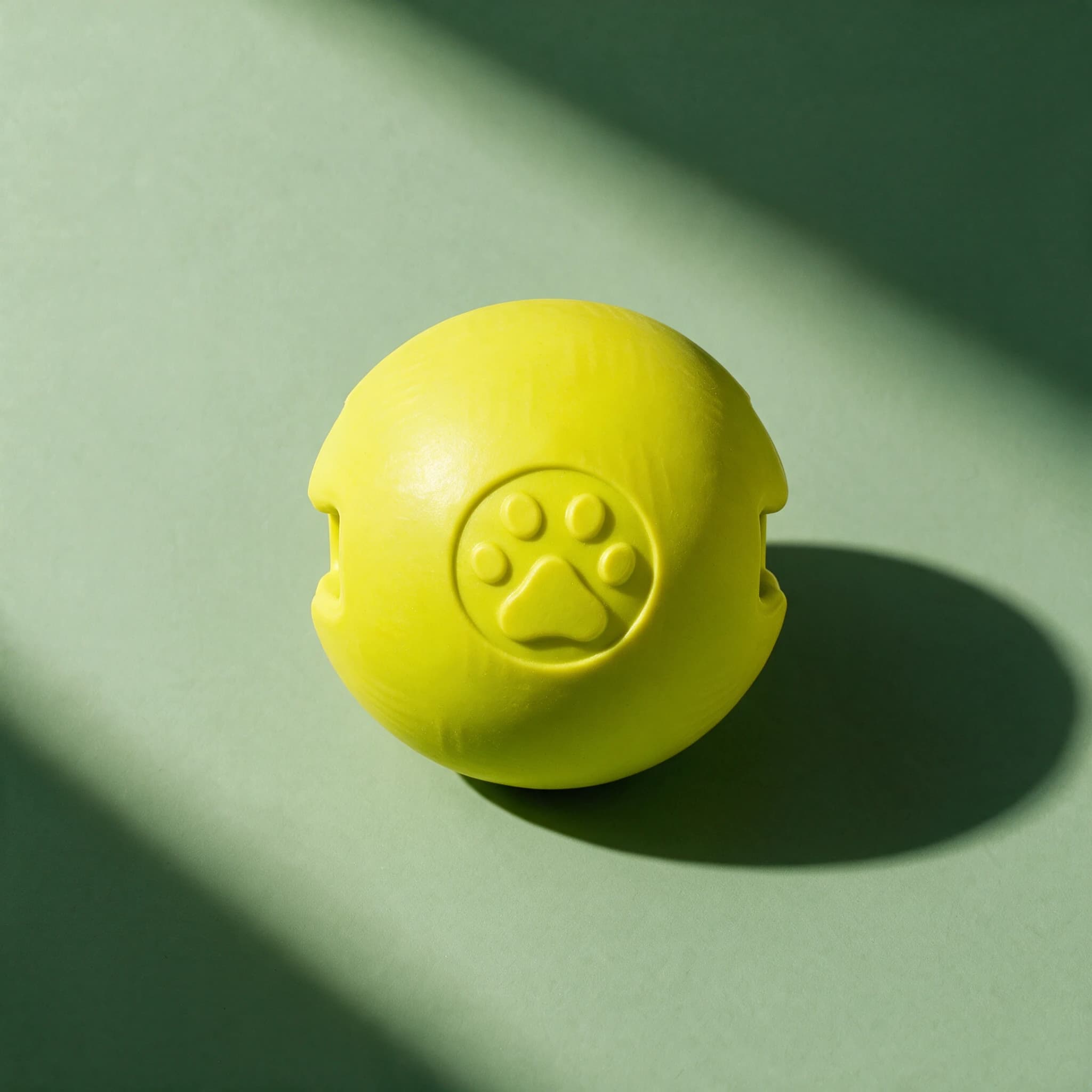 Close-up studio shot of the lime green textured PetLove Mighty Pups Foam Ball with an embossed paw print logo, photographed against a sage green background with dramatic shadow.