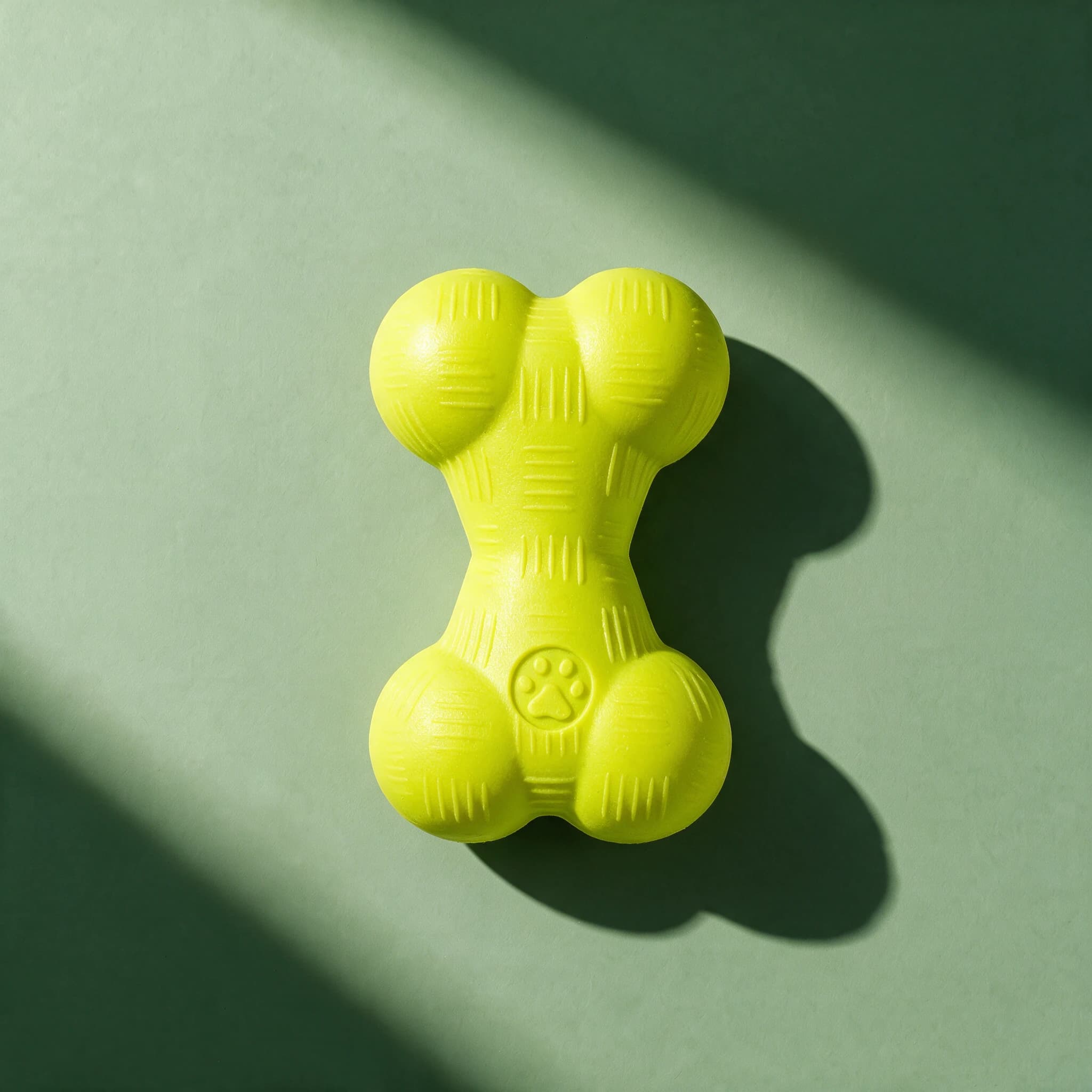 Overhead view of the lime green PetLove Mighty Pups Foam Bone toy, a ridged foam bone shape with a raised paw print detail, against a sage green background.