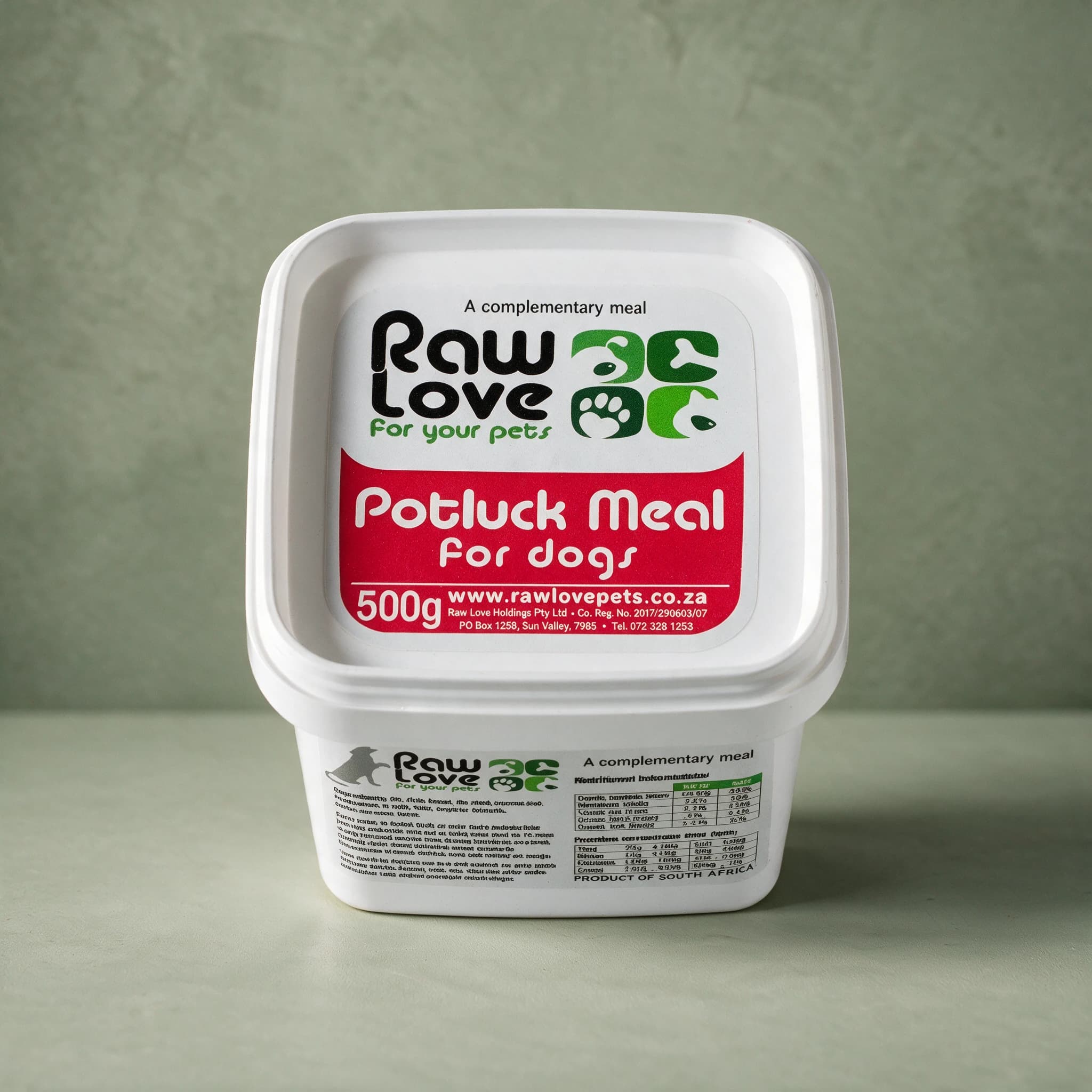 White 500g tub of Raw Love Potluck Meal for Dogs raw frozen food, red label panel with the Raw Love logo and the words 'A complementary meal', photographed against a sage green background.