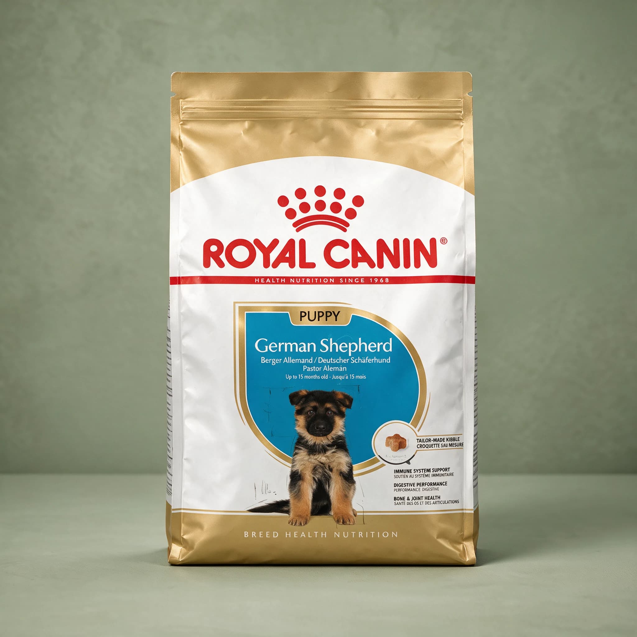 The gold Royal Canin German Shepherd Puppy dry dog food bag, featuring an illustration of a black-and-tan German Shepherd puppy and breed-specific branding, photographed against a plain sage green studio background.