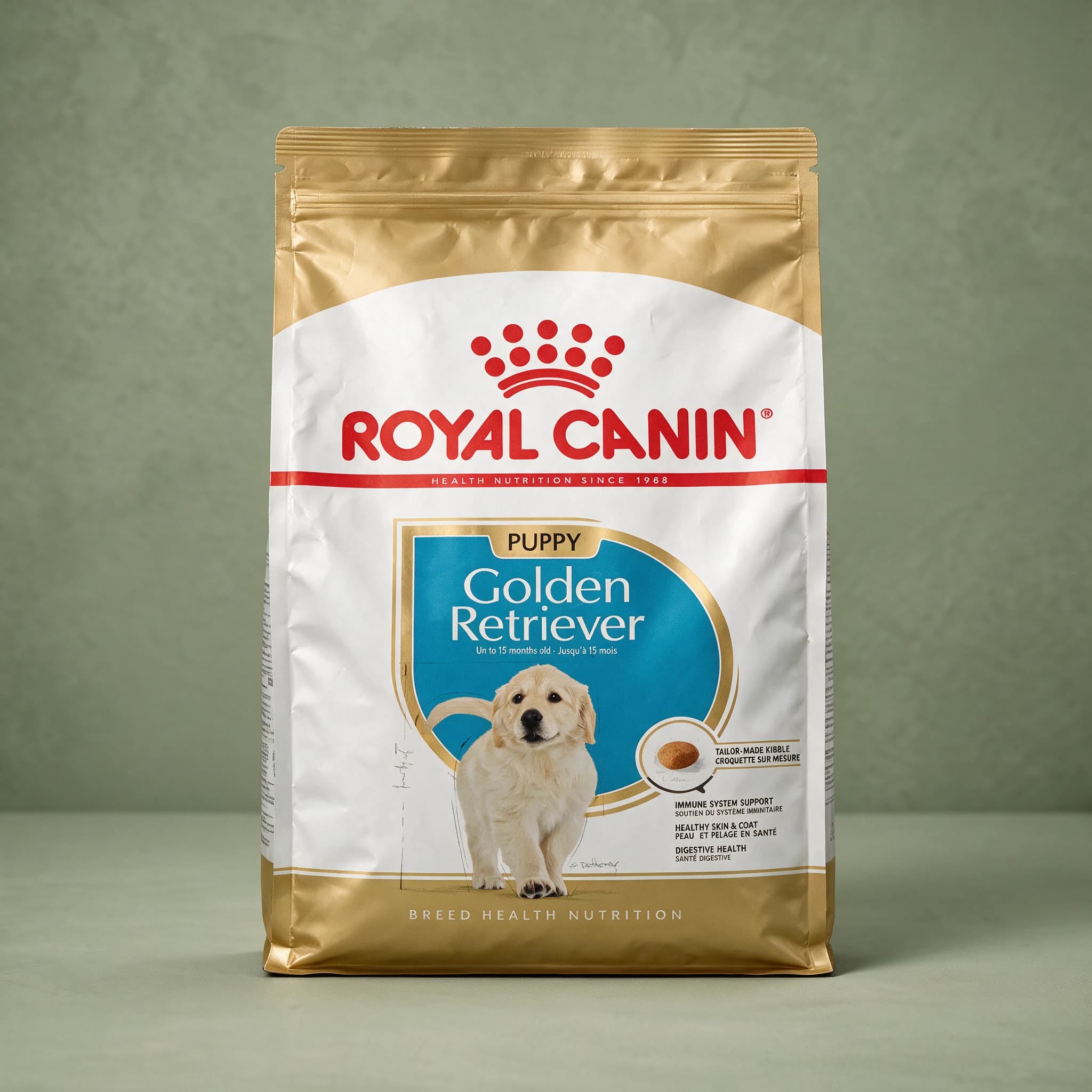 The Royal Canin Golden Retriever Puppy dry dog food bag with the red crown logo and an illustration of a Golden Retriever puppy, photographed against a plain sage green studio background.