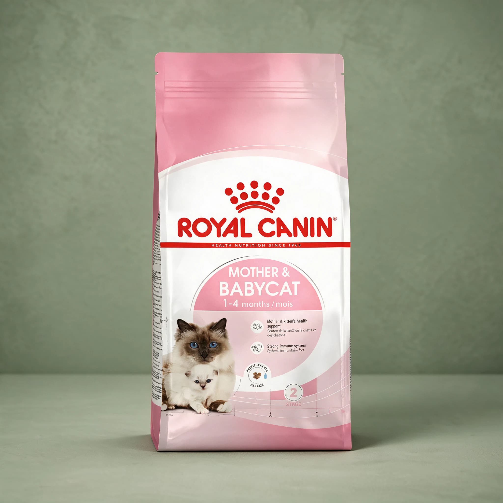 The pink and white Royal Canin Mother and Babycat dry cat food bag, featuring an illustration of a mother cat with kittens, photographed against a plain sage green studio background.