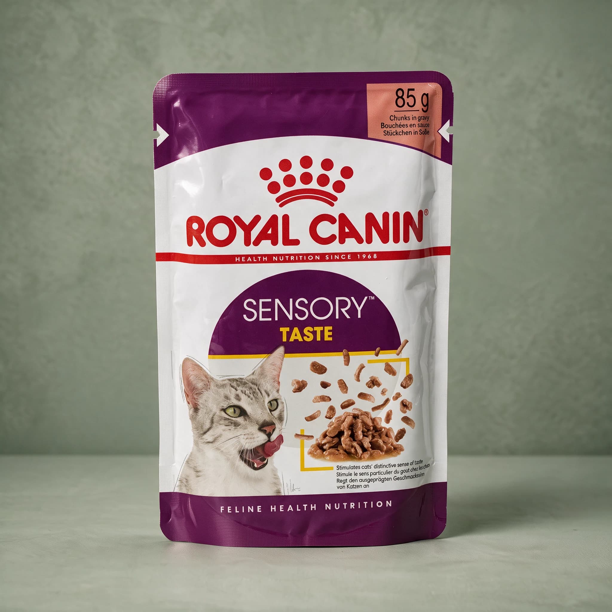 A Royal Canin Sensory Taste Adult wet cat food pouch with the red crown logo and an adult cat illustration, standing upright against a plain sage green studio background.