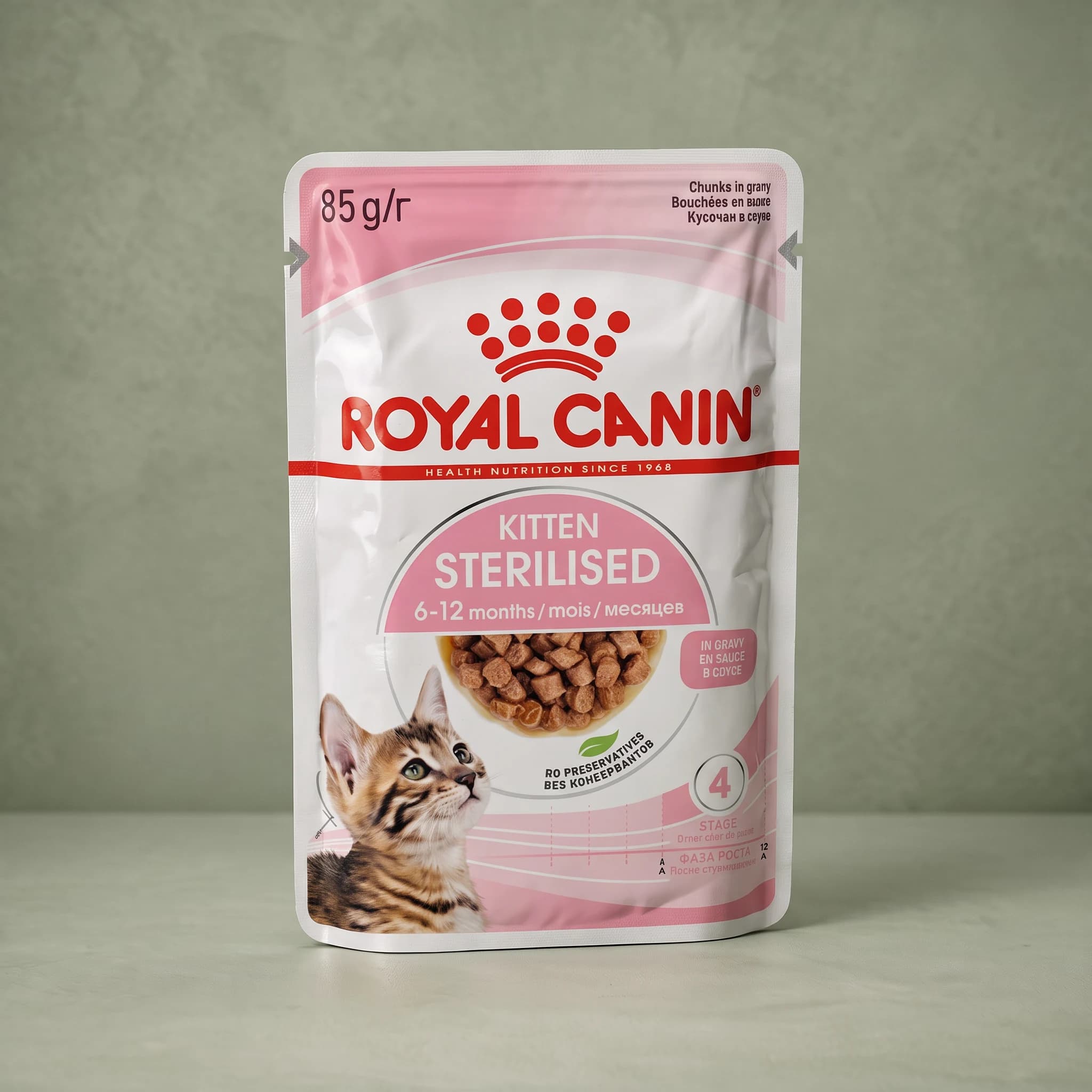 A white Royal Canin Sterilised Kitten wet cat food pouch with a kitten illustration and gravy recipe labelling, photographed against a sage green studio background.