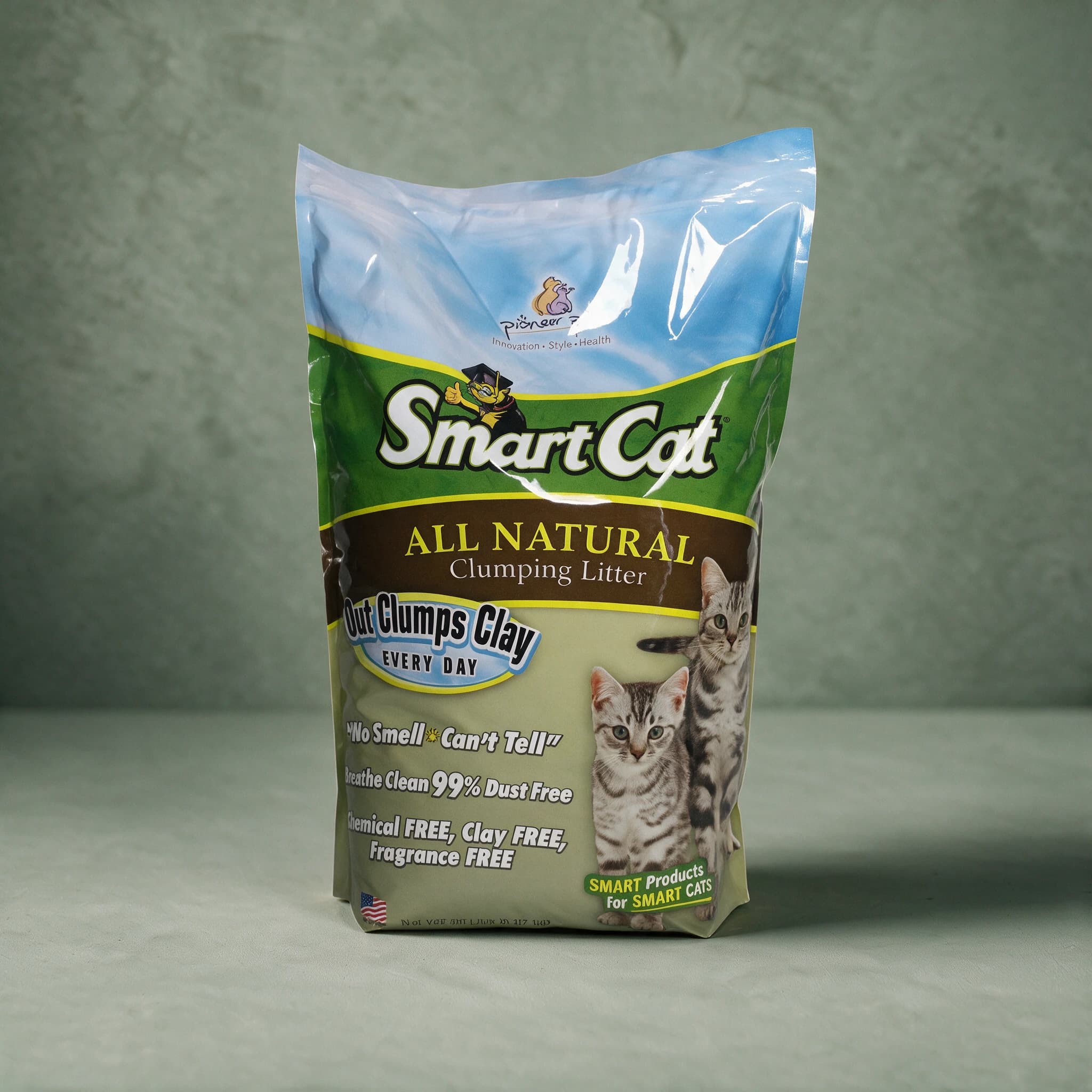 Green and cream SmartCat All Natural Clumping Litter bag with a clear blue-sky top panel, the Pioneer Pet logo, the SmartCat cartoon cat in a graduation cap, and photographs of two silver tabby cats.